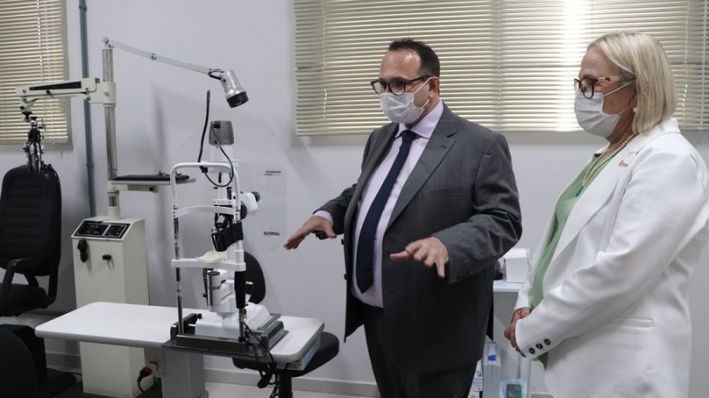 Um homem dá explicações para a Secretária Arita dentro das explicações do Hospital. Os dois estão de pé e de máscara.