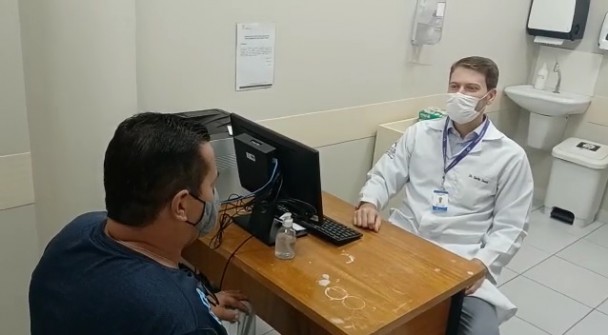 Serlio Zanol e o paciente Paulo Roberto Ferreira Costa conversam sentados, separados por uma mesa, num consultório médico. Os dois estão de máscara.
O médico cirurgião geral Serlio Zanol disse que os recursos extras para o hospital impacta diretamente na vida das pessoas
