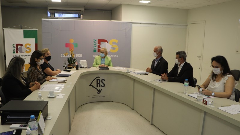 A imagem mostra a Secretária Arita e os participantes da reunião conversando. Todos estão de máscara e sentados atrás de uma mesa em formato de U. 