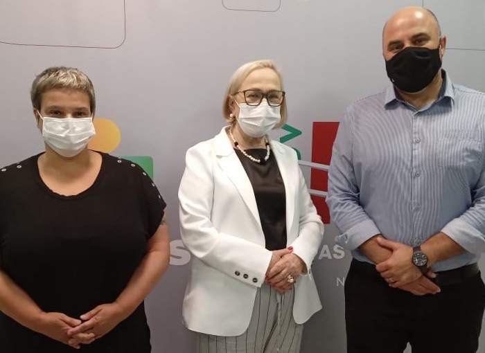 Secretária Arita, em pé, entre a diretora do DESH, Katia Brodt e o Secretário de Saúde de Bagé. Os três estão de máscara. 