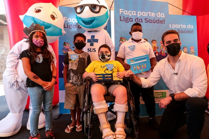 Abaixado, Governador Leite posa com quatro crianças (uma menina e três meninos), sendo uma indígena e um cadeirante. Ao lado deles, o Zé Gotinha e a Maria Gotinha.