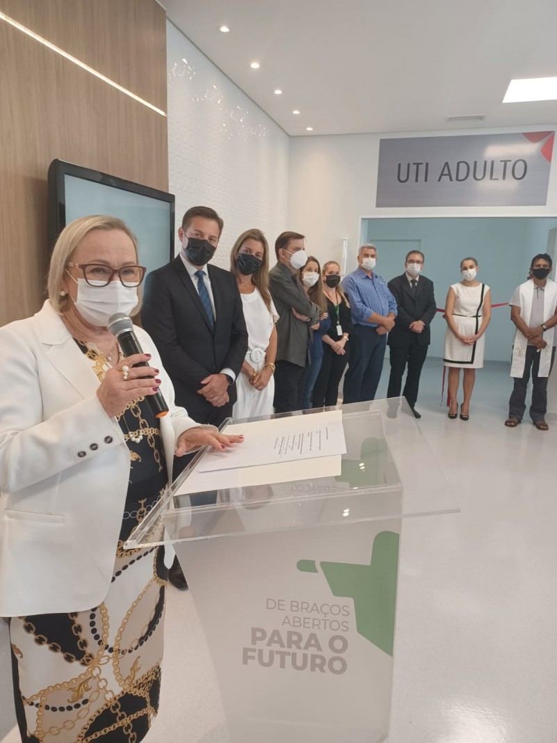 De pé, atrás de um púlpito, Secretária Arita discursa, segurando um microfone. Ao seu lado, algumas pessoas ouvem.