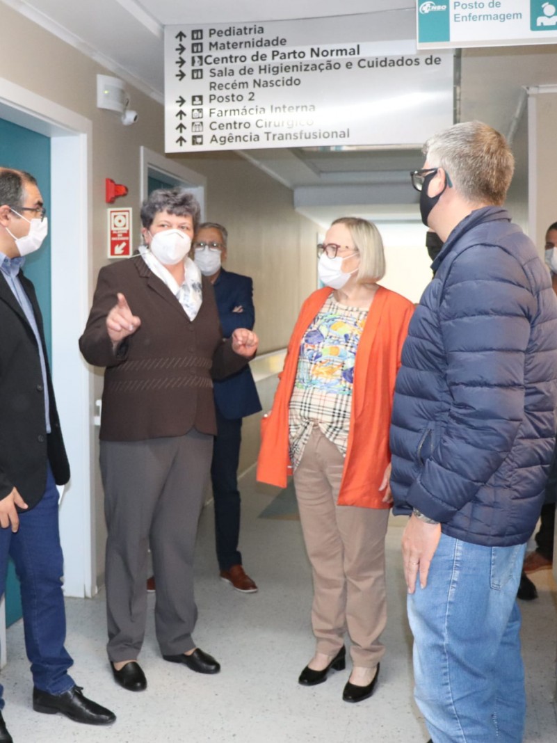A Secretária Arita ouve explicações de uma mulher. Outras pessoas acompanham a conversa. Todos estão de pé e de máscara num corredor do hospital.