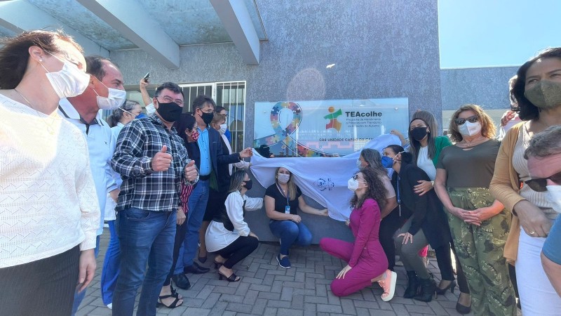 Mais de uma dezena de pessoas na rua descerrando uma placa de mais de 2 metros com o símbolo do Programa Te acolhe