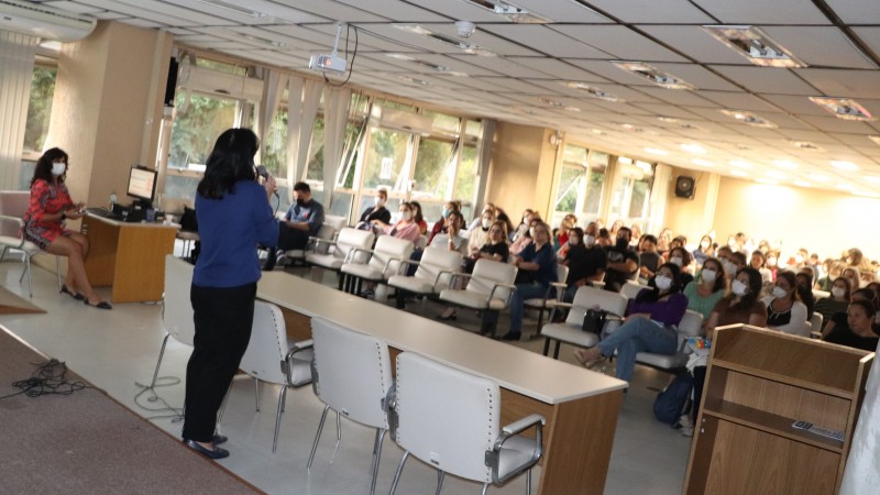 De pé, a palestrante fala ao microfone em frente à plateia, que está sentada. O evento é realizado no auditório do Centro Administrativo Fernando Ferrari, em Porto Alegre.