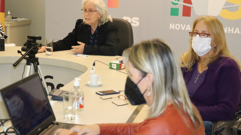 Três mulheres sentadas de uma mesa circular acompanham a live. 