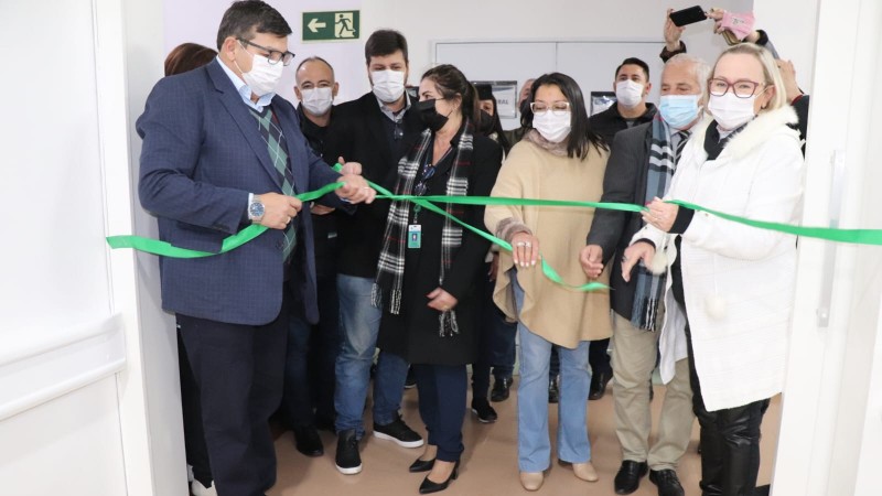 De pé, a Secretária Arita e mais algumas pessoas cortam a fita verde no hospital.