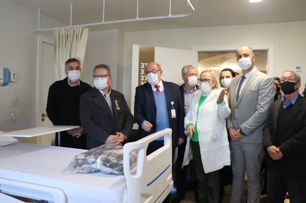 A Secretária Arita e mais algumas pessoas estão de pé e de máscara num quarto do hotel. 