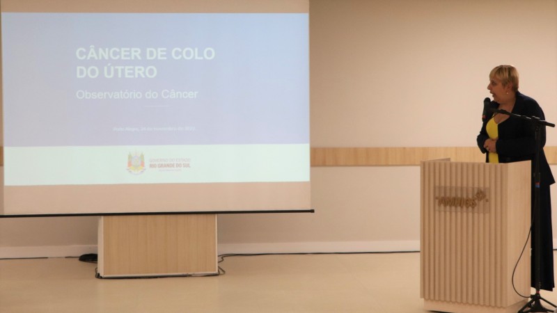 De pé e atrás de um púlpito, Ana Costa falando olhando para o telão.  