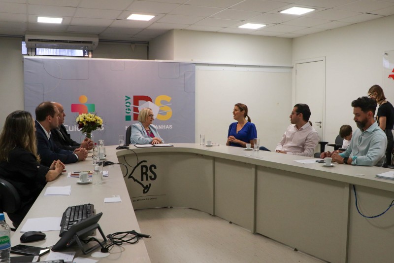A Secretária Arita está no centro de uma mesa em forma de U. Em torno dela, duas mulheres e quatro homens também participam da reunião.