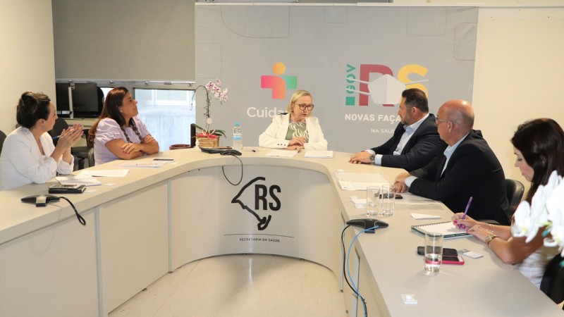 Numa mesa semicircular, com a secretária Arita ao centro, representantes da SES e da Prefeitura de Estrela