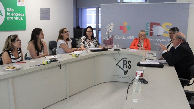 Atrás de uma mesa em formato de U, a Secretária Arita conversa com quatro mulheres e dois homens. Uma mulher e homem falam. Todo estão sentados.