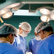 quatro profissionais de saúde com máscaras, jalecos e toucas cirúrgicas em uma sala de cirurgia