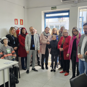 Equipe do Cerest e autoridades dentro do prédio, em um ambiente majoritariamente branco, onde está uma mesa de escritório com computador. Ao fundo uma porta e uma janela.
