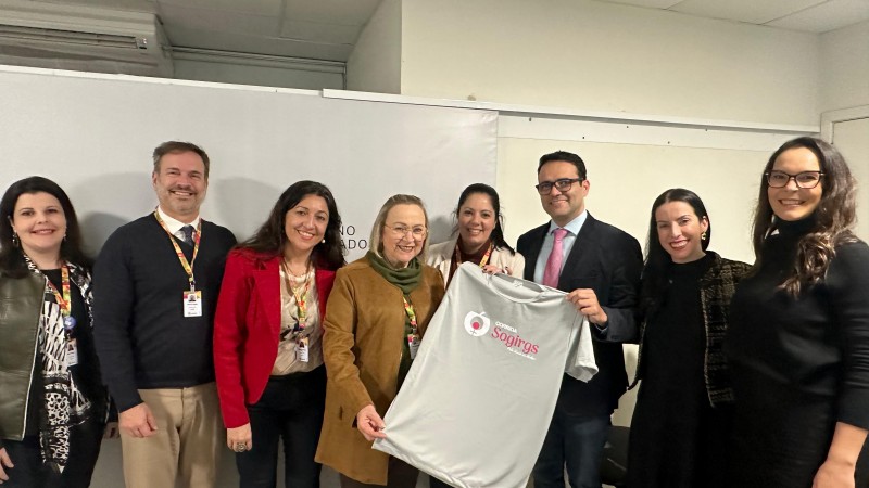 Dois homens e seis mulheres em pé, segurando uma camisa alusiva ao evento da corrida pela saúde da mulher