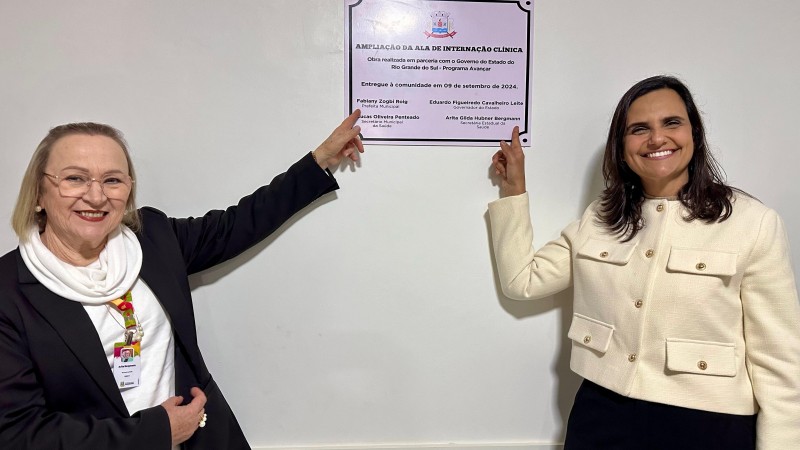 Duas mulheres em pé apontando para a placa de inauguração fixada na parede, uma delas é a secretaária da saúde Arita Bergmann e a outra é a prefeita de São José do Norte.