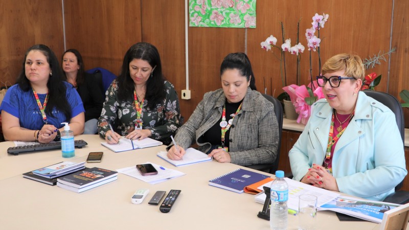  Cinco mulheres à mesa  de reuniões escrevendo relatórios olhando para frente 