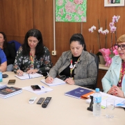  Cinco mulheres à mesa  de reuniões escrevendo relatórios olhando para frente 