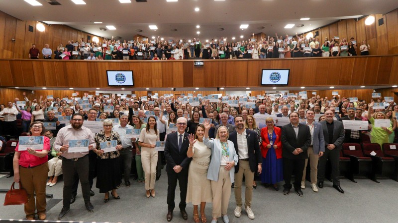 centenas de pessoas em um auditório com mezanino, algumas mostrando certificados