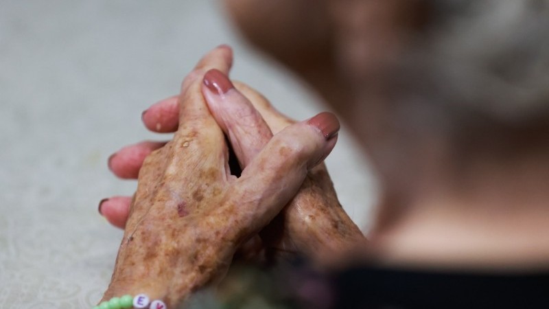 mãos de uma mulher idosa cruzadas com unhas pintadas 