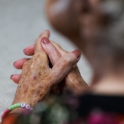 mãos de uma mulher idosa cruzadas com unhas pintadas 