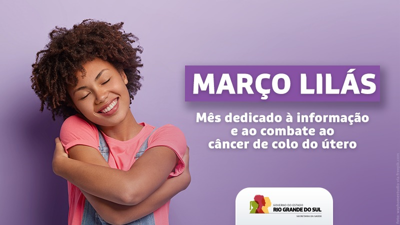 Uma mulher negra de cabelos crespos e curtos está de olhos fechados fazendo o gesto de abraçar. Ela veste uma camiseta cor de rosa. Ao lado em letras maiúsculas na cor branca está escrito: MARÇO LILÁS. Abaixo, em letras minúsculas na cor branca o letreiro segue: Mês dedicado à informação e ao combate ao câncer de colo do útero. O fundo da imagem é lilás. O logo do governo do estado está posicionado do meio para a direita da imagem.