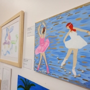 Um quadro pintado com tinta mostra a figura de duas bailarinas. A cor prevalente é azul. Ele está posto na parede branca ao lado de outras obras.
