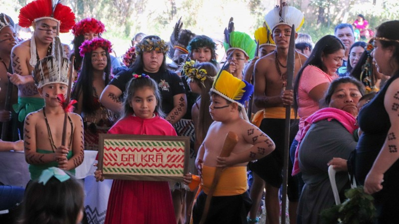 Grupo de pessoas indígenas formado por adultos, jovens e crianças, todos com adereços e roupas da cultura indígena