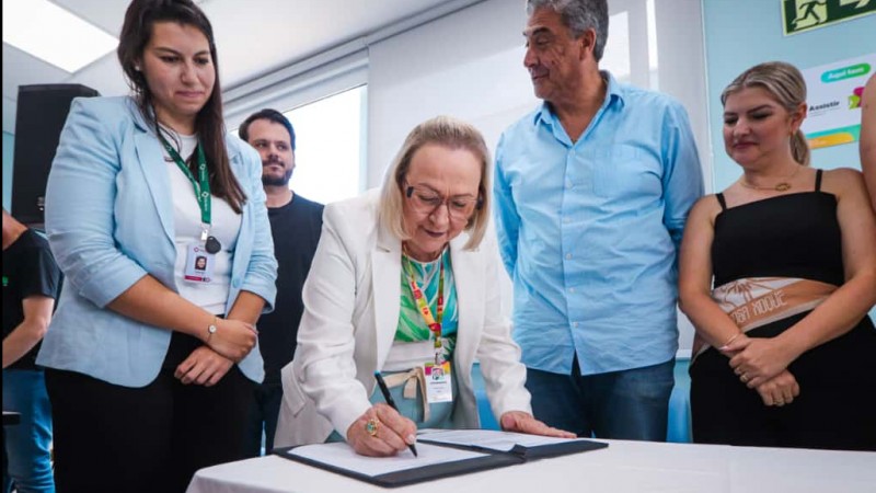 Arita Bergmann assina o conv&ecirc;nio durante a cerim&ocirc;nia, observada pelos participantes