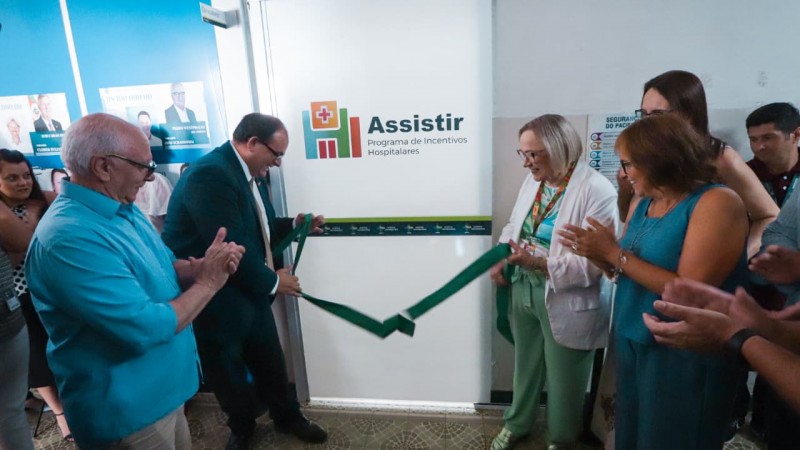 A secret&aacute;ria da Sa&uacute;de, Arita Bergmann, &agrave; direita participa do corte da fita inaugural do novo setor, tendo ao fundo a imagem, em um fundo branco do logo do programa Assistir, da Secretaria da Sa&uacute;de