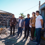 Imagem mostra grupo de pessoas em visita a uma obra, em &aacute;rea externa, com estruturas de constru&ccedil;&atilde;o ao fundo e cont&ecirc;iner &agrave; direita. As pessoas est&atilde;o reunidas, observando o local.