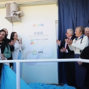Momento de inaugura&ccedil;&atilde;o institucional, com v&aacute;rias pessoas reunidas diante de uma placa identificando o CAS &ndash; Centro de Atendimento em Sa&uacute;de / TEAcolhe RS / APAE Santa Cruz do Sul &ndash; RS, parcialmente coberta por uma cortina, indicando ato oficial de descerramento.