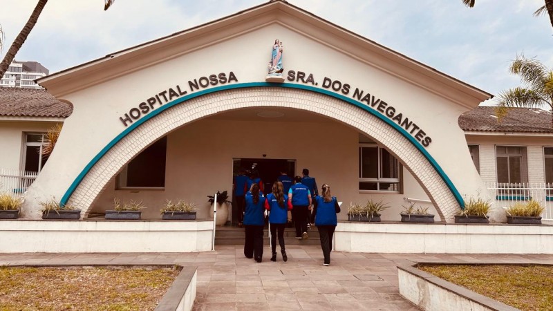 Fotografia da fachada principal do Hospital Nossa Senhora dos Navegantes. O pr&eacute;dio tem arquitetura sim&eacute;trica, com uma grande entrada em formato de arco revestida por tijolos claros. Na parte superior da fachada est&aacute; a inscri&ccedil;&atilde;o &ldquo;HOSPITAL NOSSA SRA. DOS NAVEGANTES&rdquo; e, ao centro, acima do arco, h&aacute; uma imagem religiosa instalada em um nicho.

Em primeiro plano, um caminho pavimentado conduz &agrave; entrada do hospital. Ao longo do percurso, h&aacute; canteiros com vegeta&ccedil;&atilde;o baixa e vasos distribu&iacute;dos junto &agrave; fachada. Um grupo de pessoas vestindo coletes azuis caminha em dire&ccedil;&atilde;o &agrave; porta principal do edif&iacute;cio. Nas laterais da constru&ccedil;&atilde;o s&atilde;o vis&iacute;veis janelas e, ao fundo, parte de edifica&ccedil;&otilde;es mais altas e &aacute;rvores. A imagem foi registrada durante o dia, sob ilumina&ccedil;&atilde;o natural e c&eacute;u parcialmente nublado.