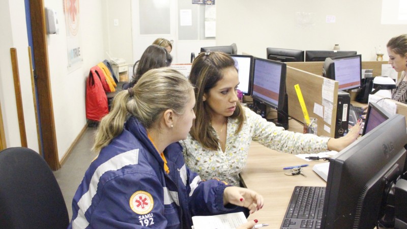 Duas atendentes do Samu conversam, sentadas na frente de um computador.