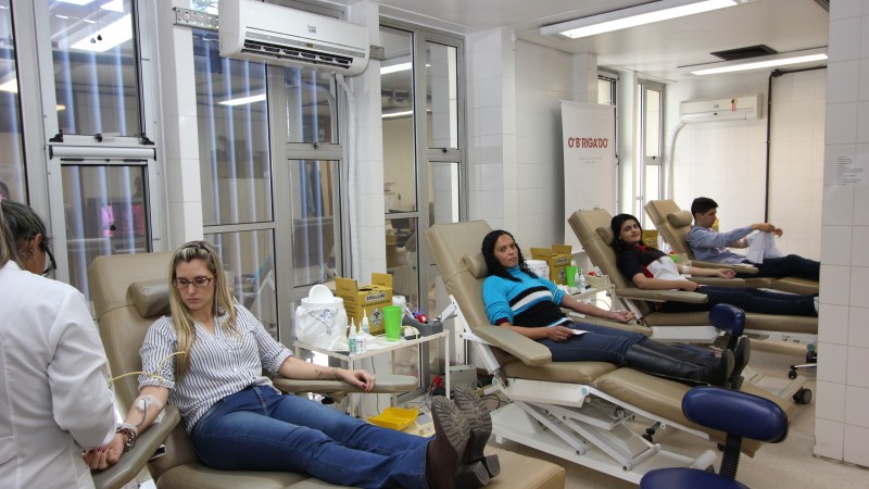 Foto mostra quatro doadores (três mulheres e um homem) sentados nas cadeiras no momento da doação. De pé, uma profissional de saúde acompanha uma doadora. 