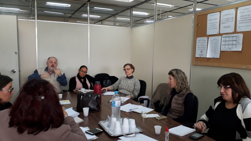 Participantes da reunião conversam sentados em torno de uma mesa redonda. 