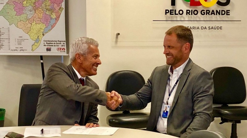 Secretário Gabbardo e Luciano, sentados, sorriem e trocam aperto de mão.