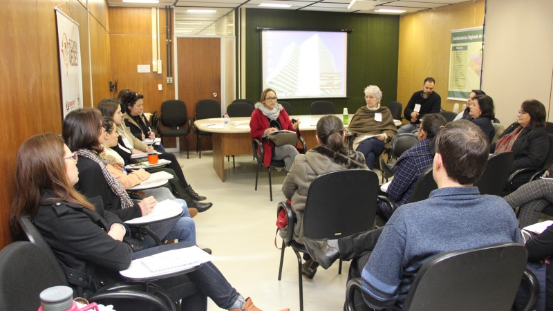 Os dois palestrantes conversam com as várias pessoas que estão na sala. Todos estão sentados. 