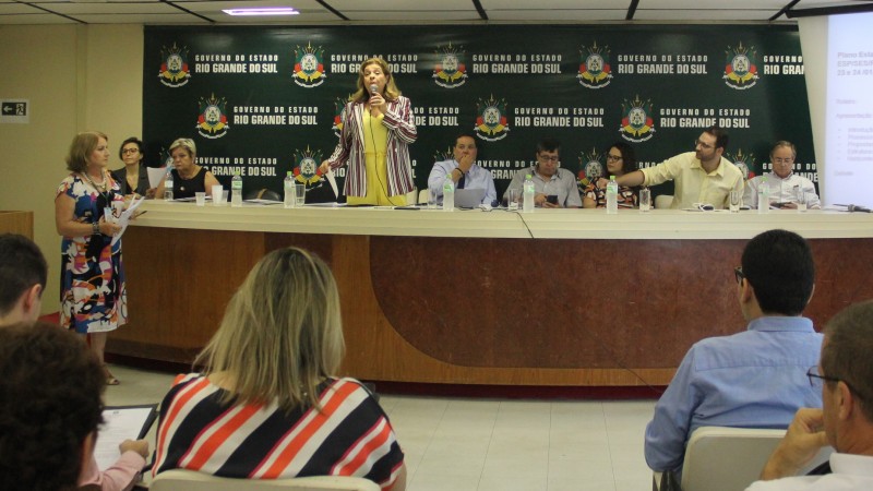 Secretária-adjunta, Aglaé Regina da Silva, fala para o público no auditório do Centro Administrativo Fernando Fernando Ferrari em Porto Alegre como coordenadora da reunião da Comissão de Gestores Bipartite. Ela está de pé e, ao
lado, algumas pessoas sentadas.