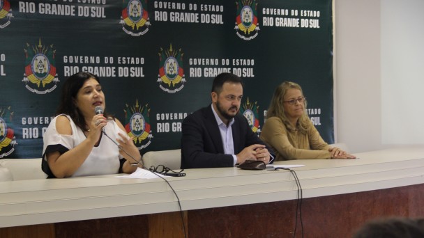 Coordenadora da seção de Saúde da Mulher fala no microfone , na mesa de abertura, ao público na abertura do Seminário sobre Violência Sexual ao lado do secretário Catarina Paladino e representante do Centro estadual de Vigilância em Saúde, Tani Ranieri