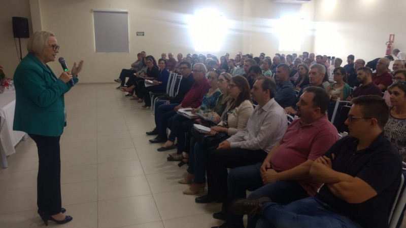 Secretária estadual da Saúde, em pé, com microfone, fala para plateia cheia