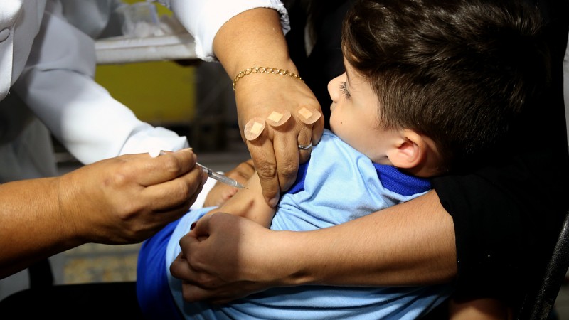 Um menino toma a vacina, de uma médica, no braço.