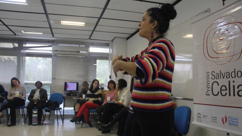 A coordenadora do PIM Gisele fala em pé para um público de mulheres sentadas em semi-círculo