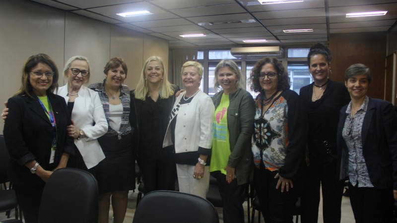Secretária Arita Bergmann em pé, acompanhada por oito mulheres que participaram da reunião. Todas sorriem. 