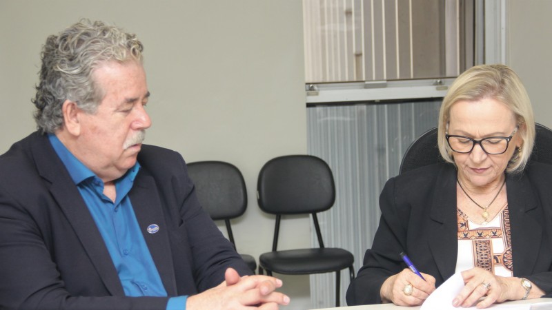 Sentados, secretária Arita e José Eri de Medeiros assinam contrato. 