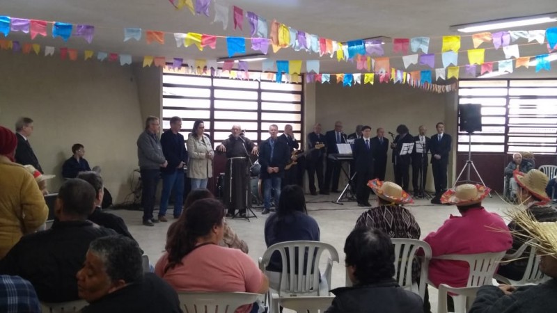 Bandeirinhas no teto, autoridades e banda de pé. A plateia está sentada.