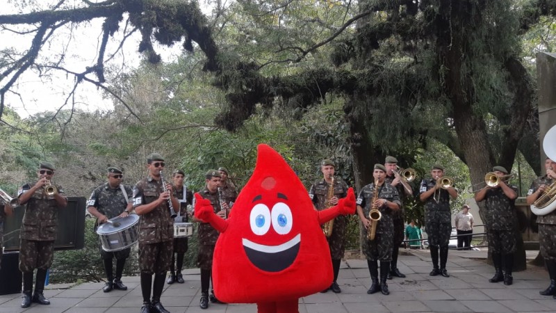 Boneco de gotinha de sangue à frente da banda do Exército, que toca.