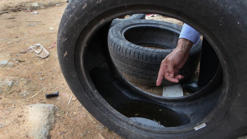 A imagem mostra uma mão masculina apontando para a água parada dentro de um pneu. 