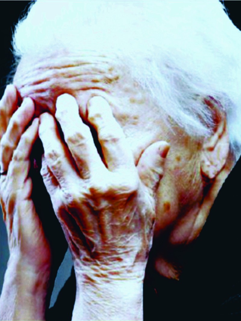Foto do rosto de uma idosa cobrindo a face com as mãos 