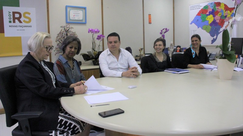 Secretária Arita assina termo. Do lado dela, Everaldina; Ronaldo; Carla e Meriana. Todos estão sentados.